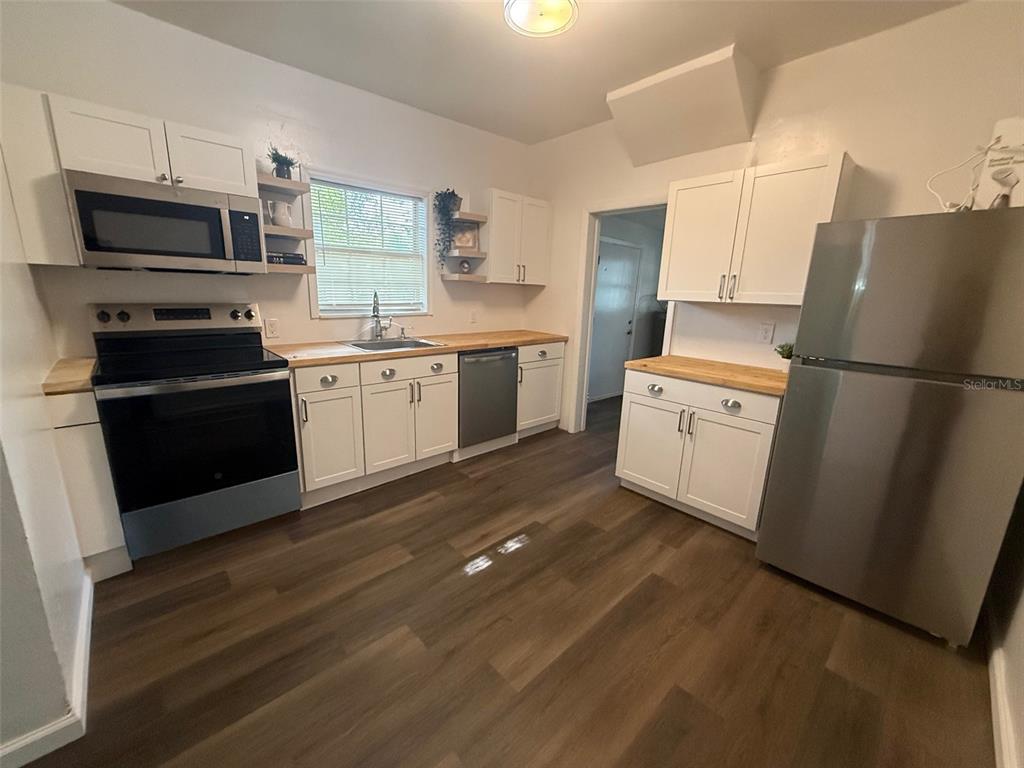 A kitchen features white cabinets, stainless steel appliances, and wood-look flooring — 1210 E 32ND AVENUE, TAMPA, FL