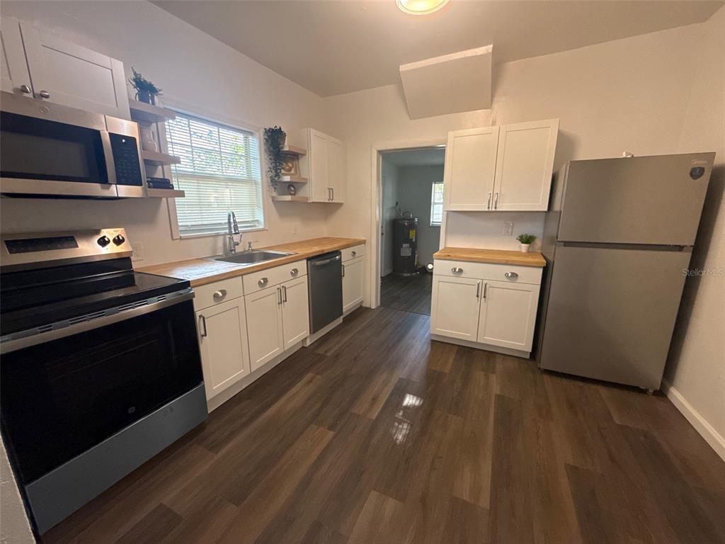 A kitchen features white cabinets, butcher block countertops, stainless steel appliances, and wood-look flooring — 1210 E 32ND AVENUE, TAMPA, FL