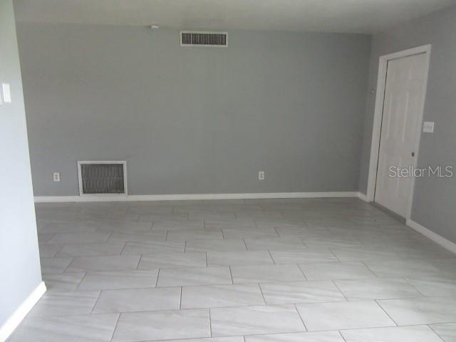 An empty room with gray walls, white baseboards, and light-colored rectangular floor tiles — 890 7TH AVENUE NE, LARGO, FL