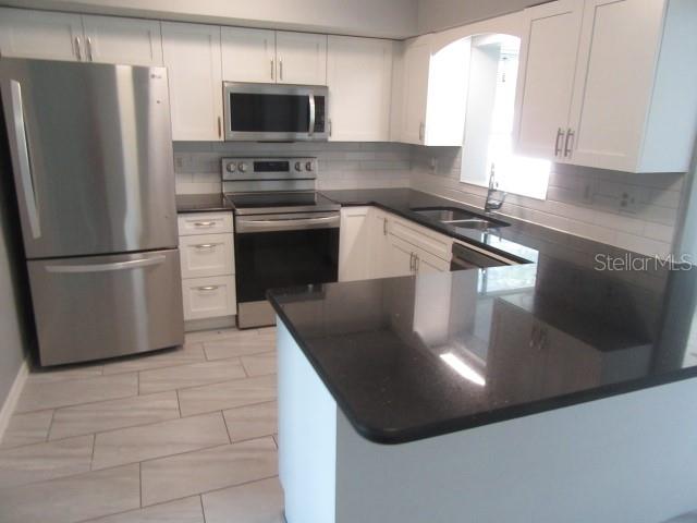 A kitchen features white cabinets, stainless steel appliances, and a black countertop peninsula — 890 7TH AVENUE NE, LARGO, FL