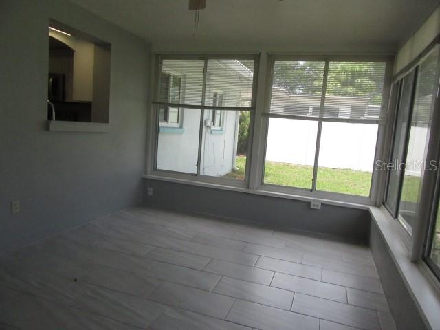 A sunroom with light gray walls, tile flooring, and large windows overlooking a backyard — 890 7TH AVENUE NE, LARGO, FL