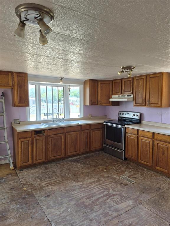 A kitchen with wood cabinets, a stainless steel stove, and an unfinished plywood floor — 9285 SE 140TH PLACE, SUMMERFIELD, FL