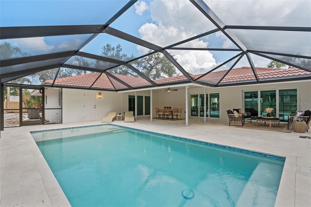 A screened-in swimming pool patio with lounge chairs, outdoor dining, and seating areas — 670 VENICE LANE, SARASOTA, FL