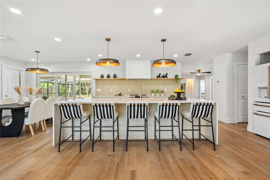 A modern kitchen features a large island with striped bar stools and light wood flooring — 670 VENICE LANE, SARASOTA, FL