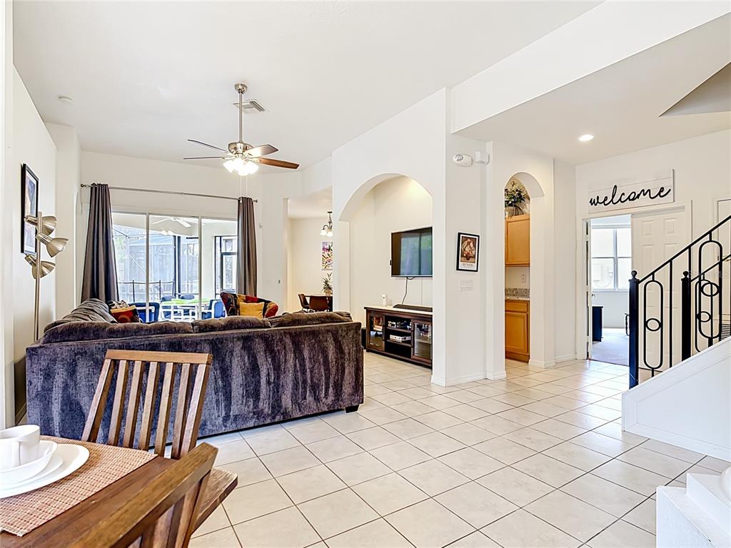 A living room with a large sofa, tile flooring, and an arched entryway to a kitchen — 672 ORISTA DR, DAVENPORT, FL