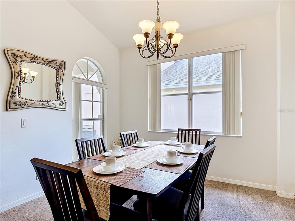 A dining room features a wooden table with six place settings, a chandelier, and a mirror — 672 ORISTA DR, DAVENPORT, FL