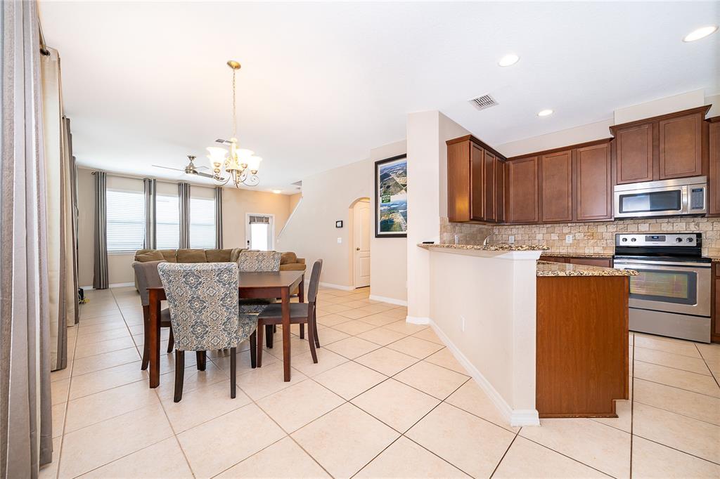An open-concept kitchen and dining area with tile floors, wooden cabinets, and stainless steel appliances — 8641 BROOKVALE DRIVE, WINDERMERE, FL