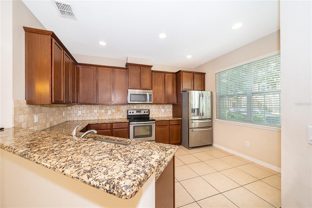 A kitchen with dark wood cabinets, granite countertops, stainless steel appliances, and tile flooring — 8641 BROOKVALE DRIVE, WINDERMERE, FL