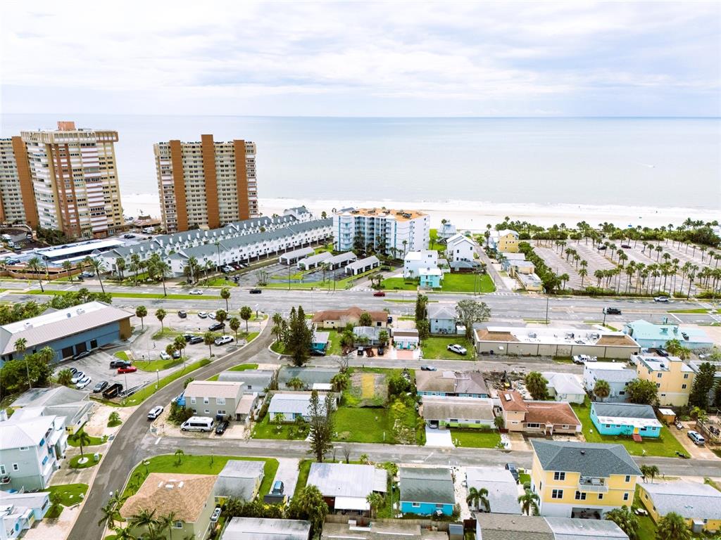 An aerial view shows a coastal neighborhood with residential houses, parking lots, and nearby hotels — 18005 1ST STREET E, ST PETERSBURG, FL