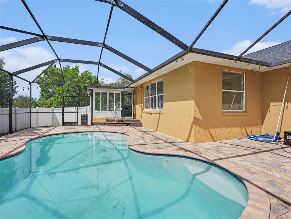 A backyard swimming pool with a screened-in enclosure and a tan stucco house exterior — 808 CHAMBERLAIN LOOP, LAKE WALES, FL