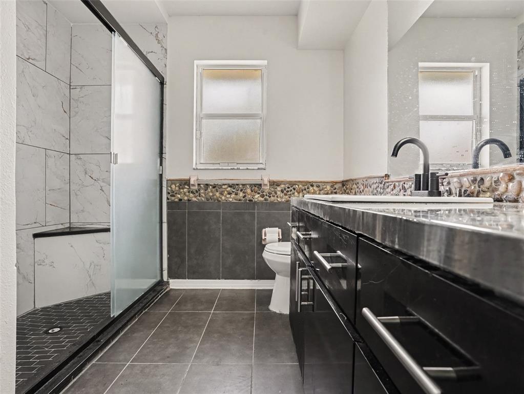 A bathroom features a glass-enclosed shower, a black vanity, and a pebble-tiled backsplash — 808 CHAMBERLAIN LOOP, LAKE WALES, FL