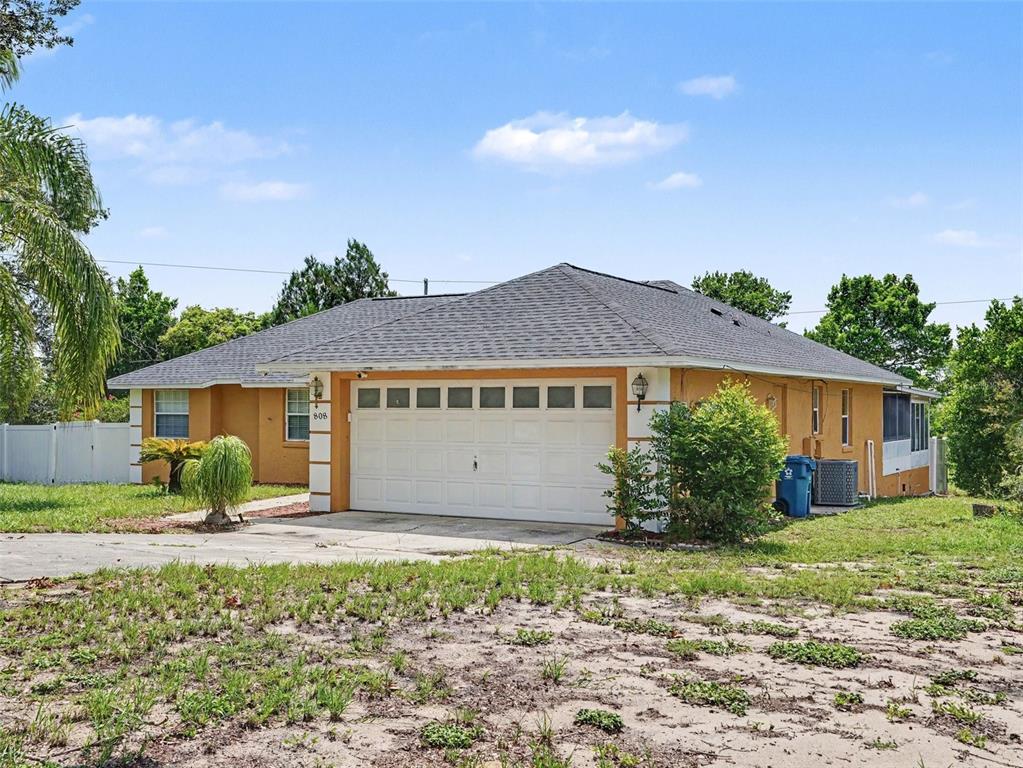 A single-story house with an orange stucco exterior, a two-car garage, and a shingled roof — 808 CHAMBERLAIN LOOP, LAKE WALES, FL