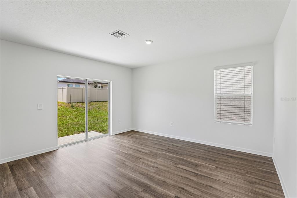 An empty room with white walls, wood-look flooring, a sliding glass door, and one window — 5614 BROOK LANE, HAINES CITY, FL