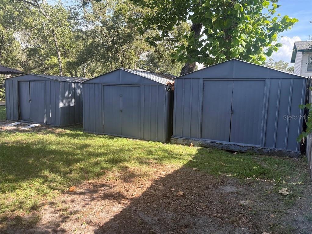 Three metal storage sheds stand in a grassy backyard under large trees — 1680 JAGUAR CIRCLE, APOPKA, FL