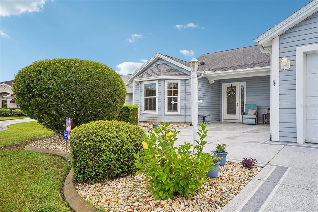 A light blue house with a concrete patio, landscaping, and a white front door — 2608 CASSO COURT, THE VILLAGES, FL