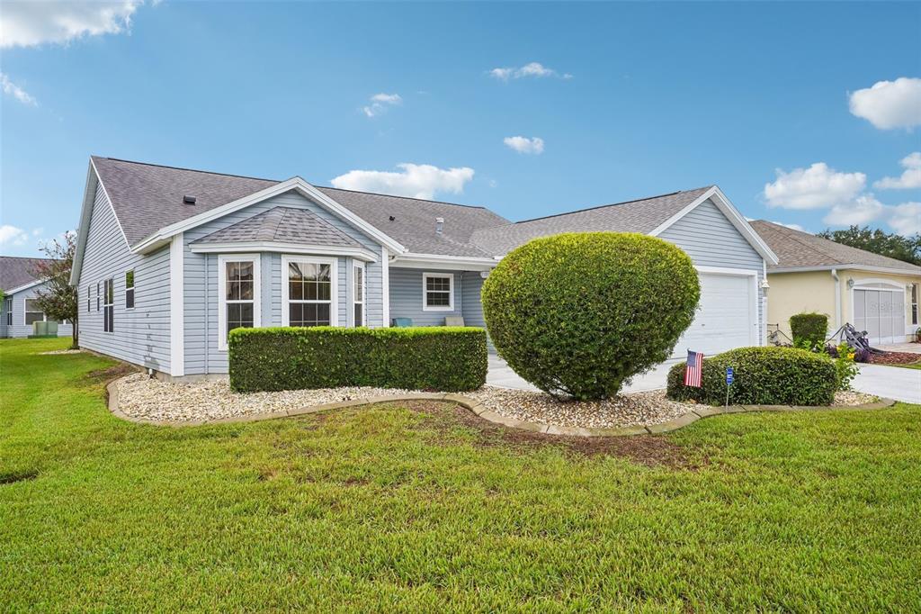 A light blue single-story house with a garage, manicured hedges, and a gravel garden bed — 2608 CASSO COURT, THE VILLAGES, FL