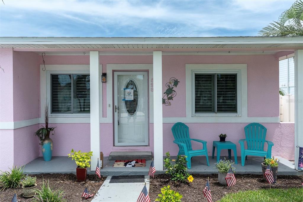 A pink house exterior features a front porch with two teal chairs and American flags — 528 77TH AVENUE, ST PETE BEACH, FL