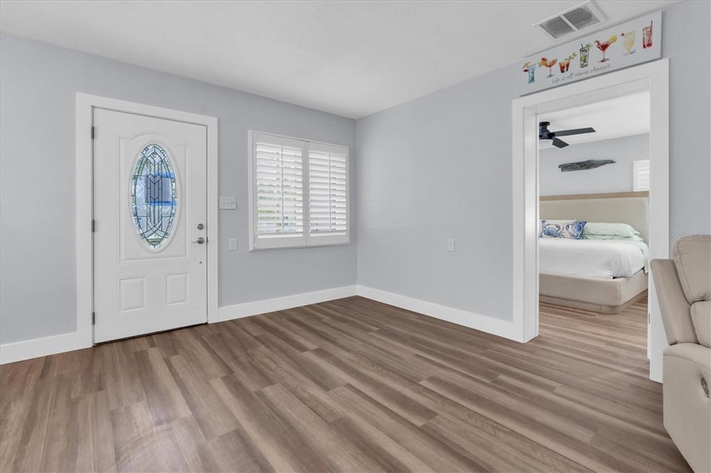 An interior view of a room with wood-look flooring, a white front door, and a bedroom — 528 77TH AVENUE, ST PETE BEACH, FL