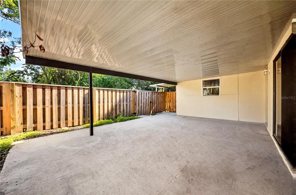 A covered concrete patio features a white ceiling and a wooden privacy fence — 2906 ASH DRIVE, LEESBURG, FL