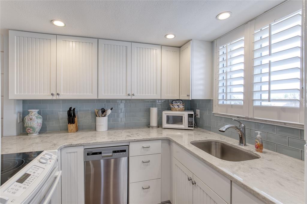 A kitchen with white beadboard cabinets, light stone countertops, and a blue subway tile backsplash — 935 OCEAN SHORE BOULEVARD UNIT 2170, ORMOND BEACH, FL