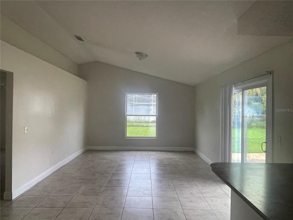 An empty living room features vaulted ceilings, tile flooring, a window, and sliding glass doors — 820 BLANC COURT, KISSIMMEE, FL