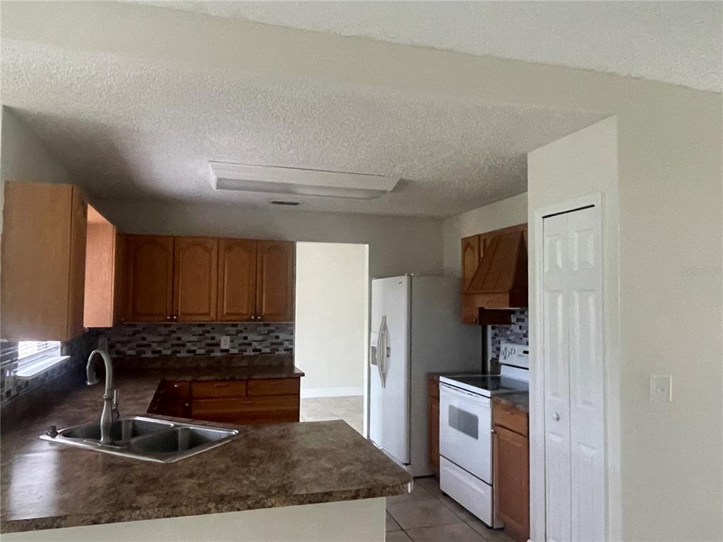 A kitchen features wood cabinets, laminate countertops, a double sink, and white appliances — 820 BLANC COURT, KISSIMMEE, FL