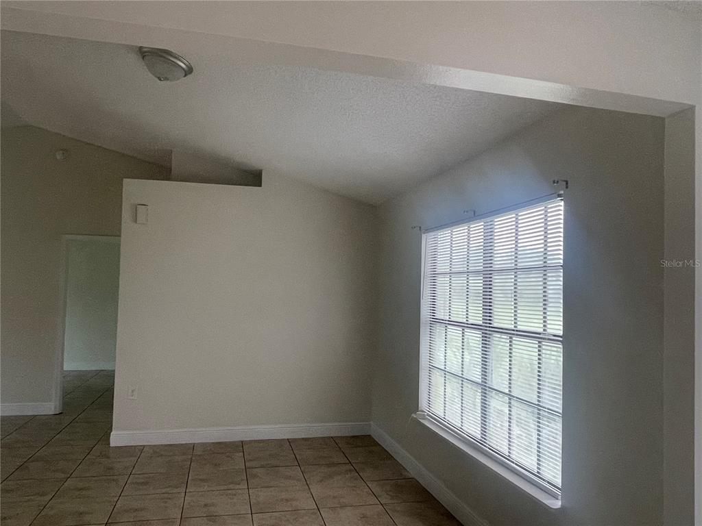 An empty room features tiled flooring, a vaulted ceiling, and a window with blinds — 820 BLANC COURT, KISSIMMEE, FL