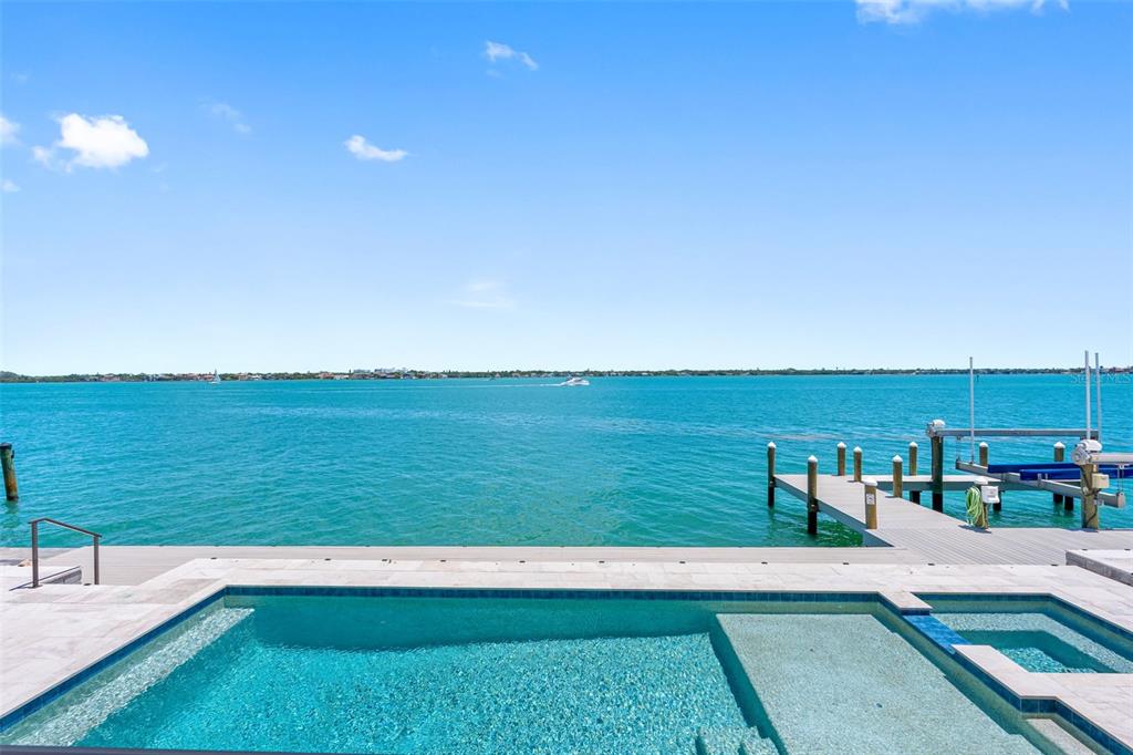 An infinity pool overlooks a bay with a private boat dock under a blue sky — 487 MEADOW LARK DR, SARASOTA, FL