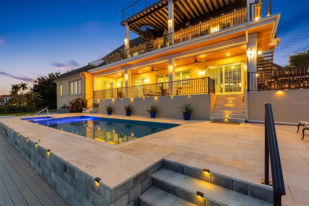 A multi-story house exterior features a raised pool deck, stone patio, and illuminated staircases — 487 MEADOW LARK DR, SARASOTA, FL
