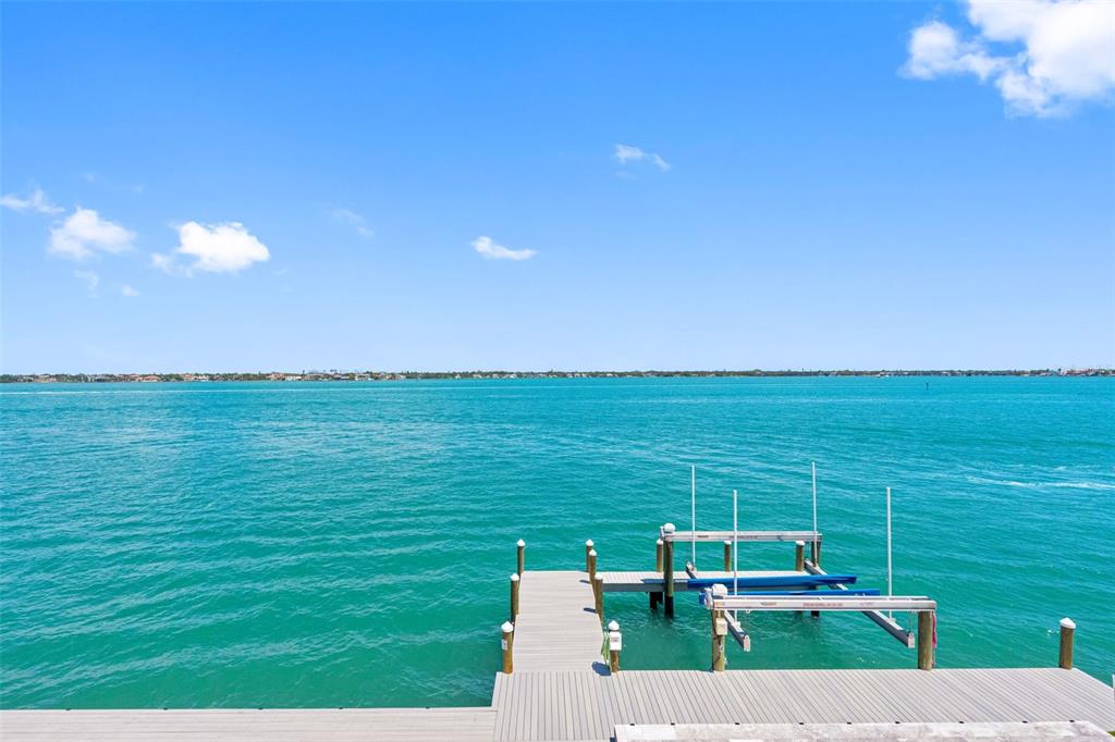 A wooden dock with a boat lift extends into a bright blue body of water — 487 MEADOW LARK DR, SARASOTA, FL