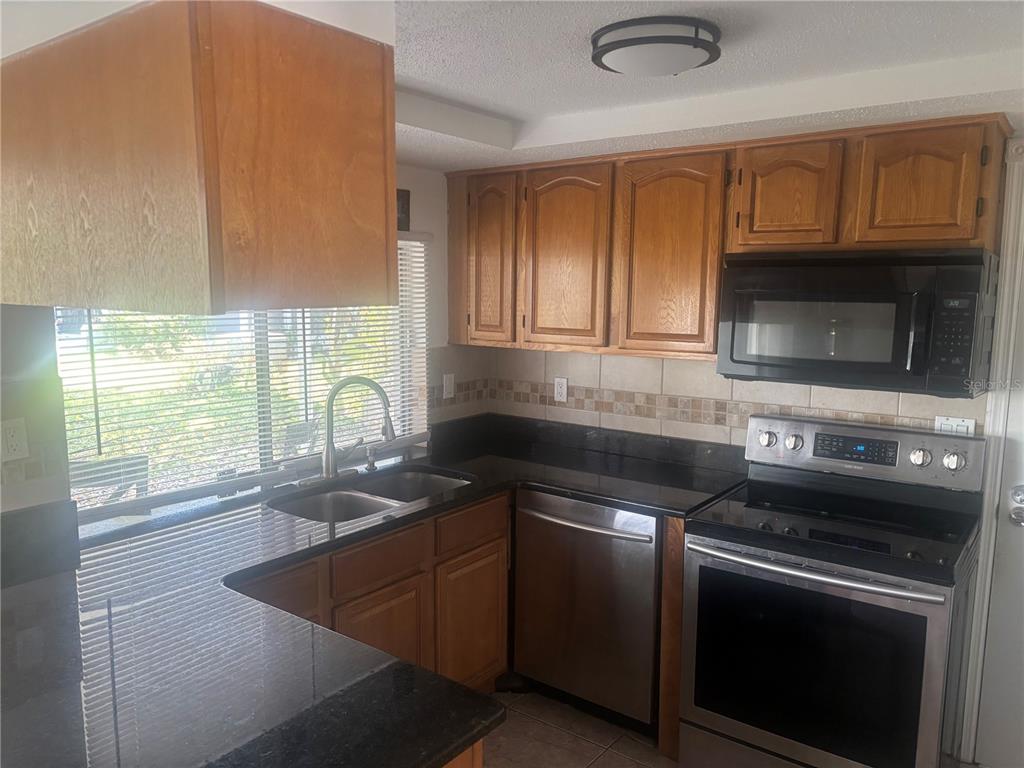 A kitchen features wood cabinets, black countertops, stainless steel appliances, and a double sink — 8302 SPLIT RAIL LANE, HUDSON, FL