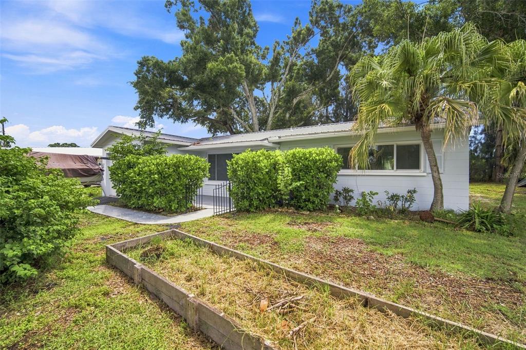 A single-story house with a white exterior, a metal roof, and a raised garden bed — 6100 35TH AVENUE N, ST PETERSBURG, FL