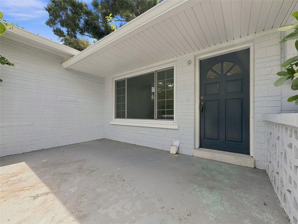 A covered concrete porch leads to a dark blue front door next to a large window — 6100 35TH AVENUE N, ST PETERSBURG, FL