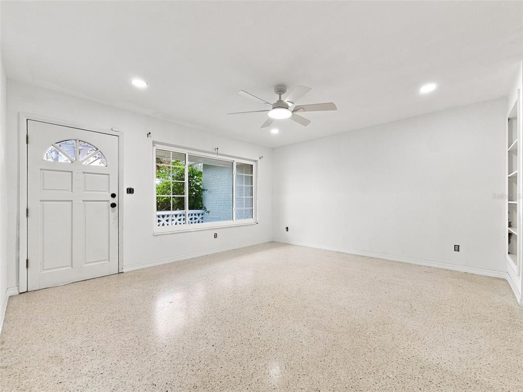 A bright, empty room features white walls, a ceiling fan, and speckled terrazzo flooring — 6100 35TH AVENUE N, ST PETERSBURG, FL