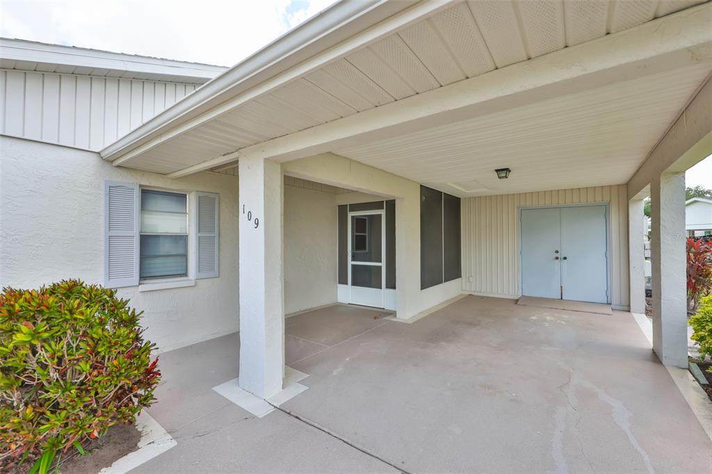 A covered carport area features a concrete floor, a white support pillar, and double doors — 109 GLENDOWER CIRCLE, SUN CITY CENTER, FL