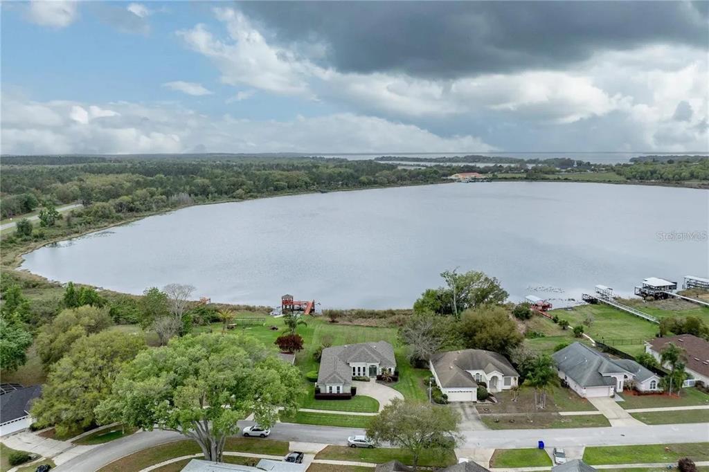 An aerial view shows houses along a lakefront with docks under a cloudy sky — 3804 BAYSHORE CIRCLE, TAVARES, FL