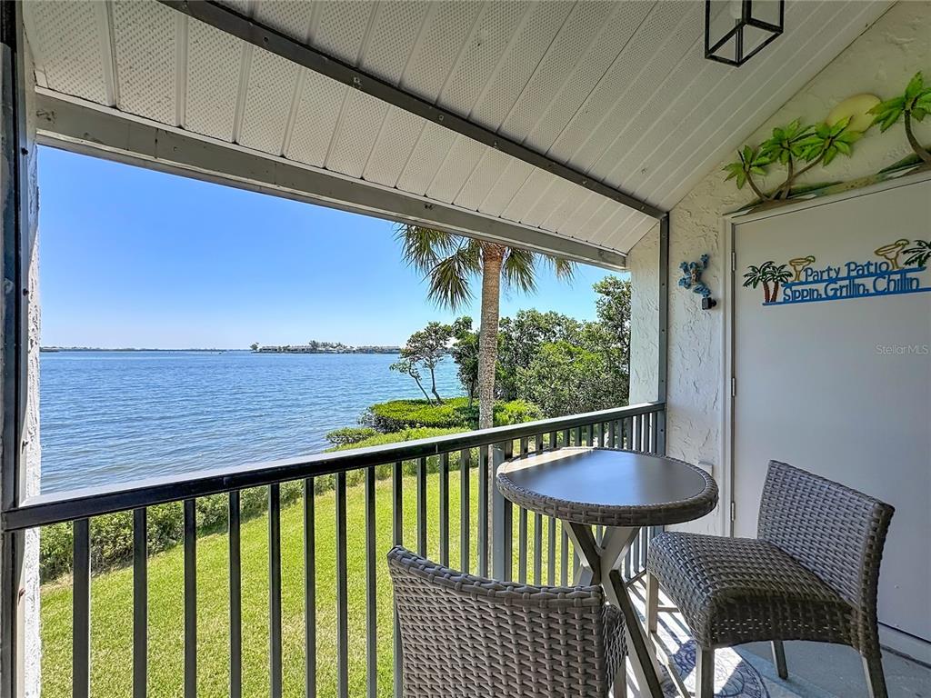 A covered balcony features a small round table, two chairs, and a view of water — 1801 GULF DRIVE N UNIT 293, BRADENTON BEACH, FL