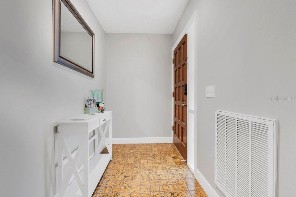 An entryway features a white console table, a wall mirror, and a brown wooden door — 5395 EMERALD ISLE DRIVE UNIT 1011, ORLANDO, FL