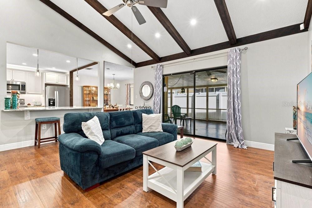 A living room features a blue sofa, wood floors, vaulted ceilings with beams, and sliding doors — 5395 EMERALD ISLE DRIVE UNIT 1011, ORLANDO, FL