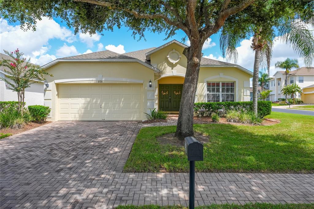 A yellow single-story house features a paved driveway, a two-car garage, and a large tree — 358 LANCASTER DR, DAVENPORT, FL