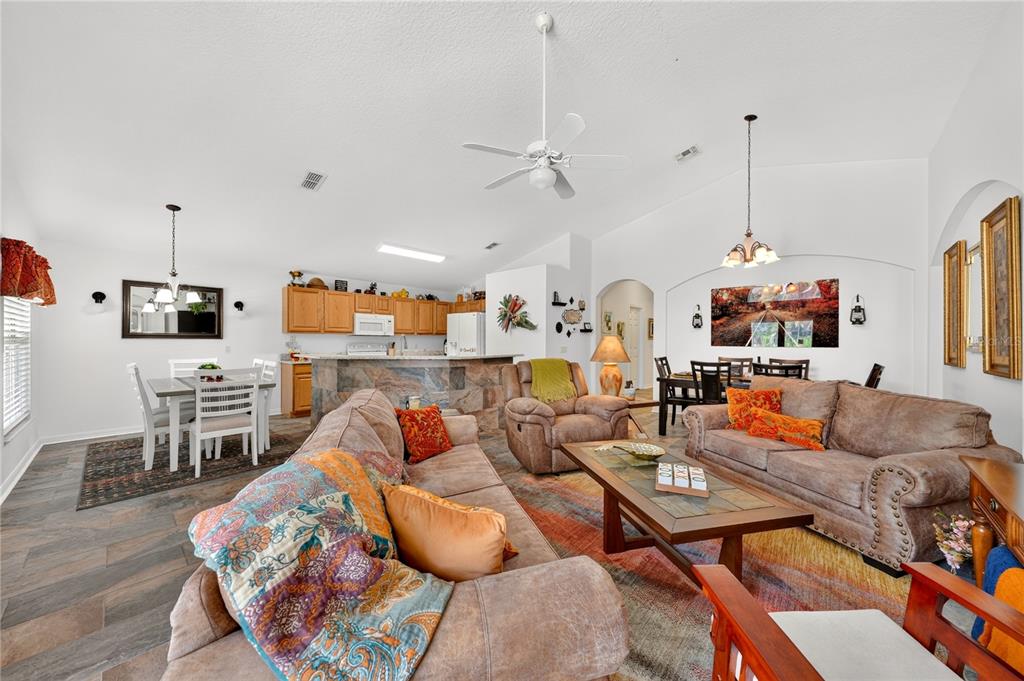 An open-concept living and dining area features tile floors, wood cabinets, and neutral furniture — 358 LANCASTER DR, DAVENPORT, FL