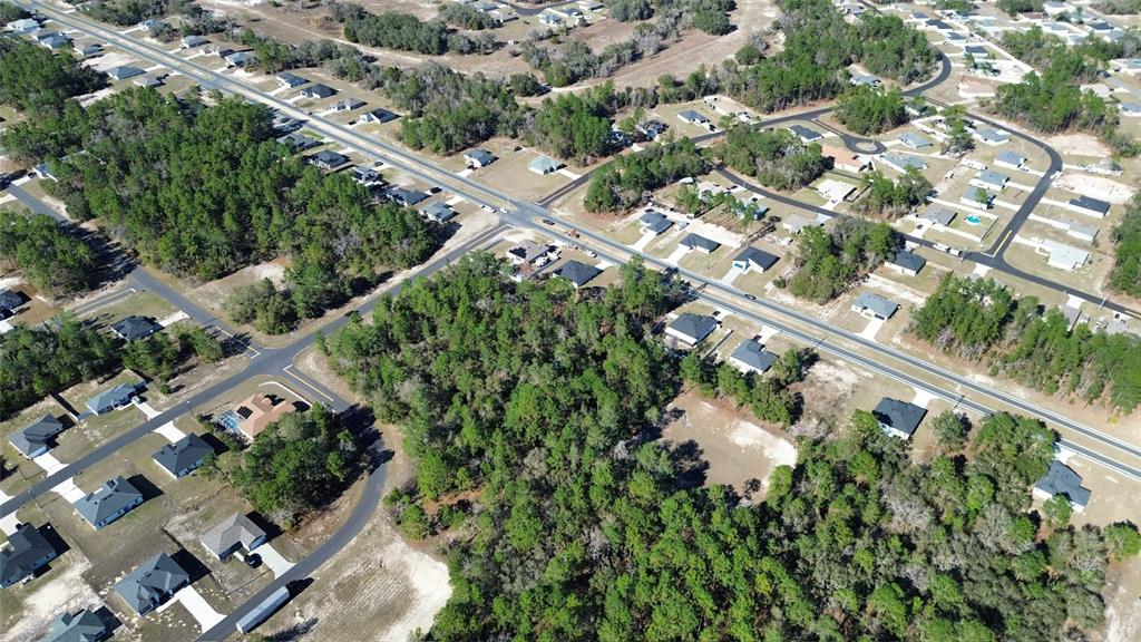An aerial view shows a suburban neighborhood with houses, paved roads, and surrounding wooded areas — LOT 11 MARION OAKS PASS, OCALA, FL