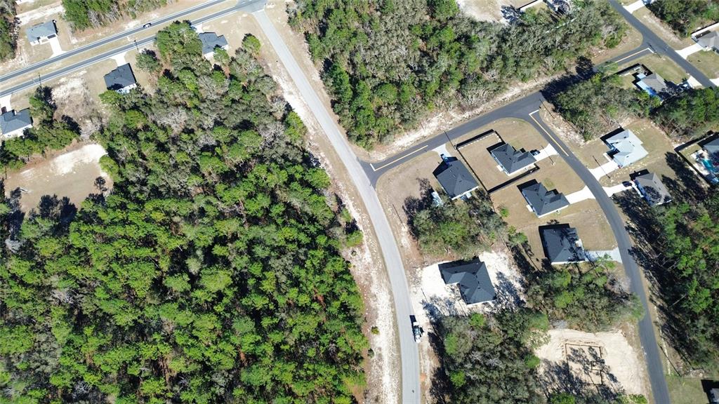 An aerial view shows a suburban neighborhood with houses, paved roads, and surrounding wooded areas — LOT 11 MARION OAKS PASS, OCALA, FL