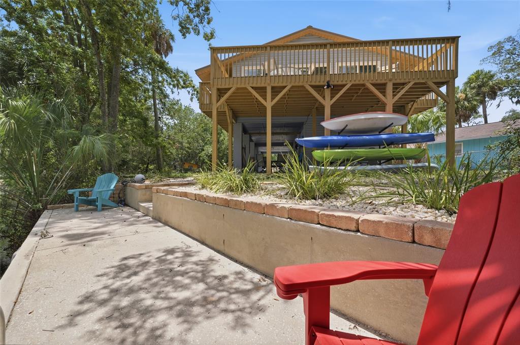 A concrete patio with a retaining wall, outdoor chairs, and stacked kayaks beneath a raised deck — 8180 ANCHOR POINT DRIVE, WEEKI WACHEE, FL