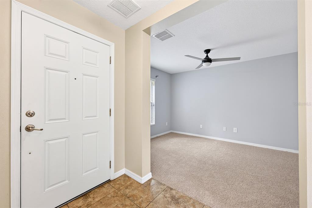 An entryway features a carpeted staircase, a white front door, and tan tile flooring — 2564 ABEY BLANCO DRIVE, ORLANDO, FL
