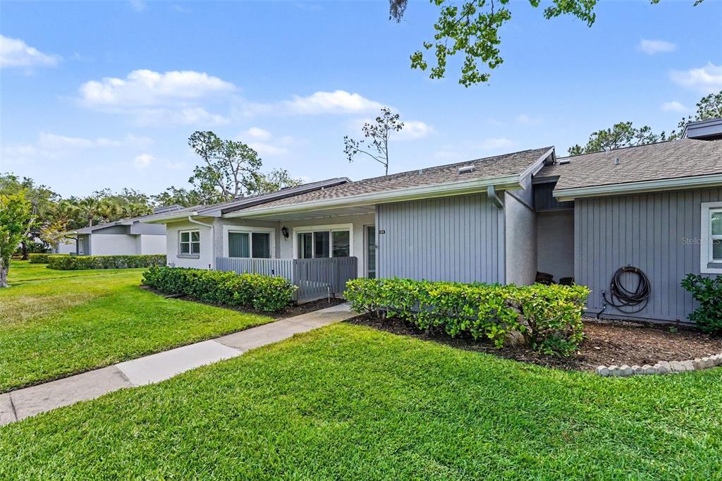 A single-story gray house with a small patio and manicured landscaping under a blue sky — 230 BALSAM DRIVE, OLDSMAR, FL