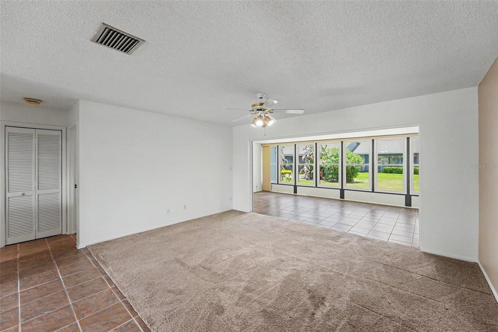 A living room with beige carpet, white walls, a ceiling fan, and a tiled sunroom — 230 BALSAM DRIVE, OLDSMAR, FL