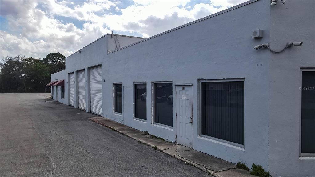 A low-rise, light-colored industrial building features multiple roll-up doors and windows along a paved lot — 415 ANGLE ROAD, FORT PIERCE, FL