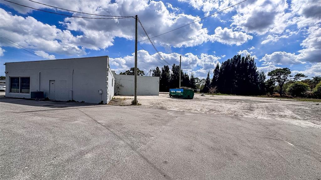 A white commercial building stands next to a large, unpaved lot with a green dumpster — 415 ANGLE ROAD, FORT PIERCE, FL