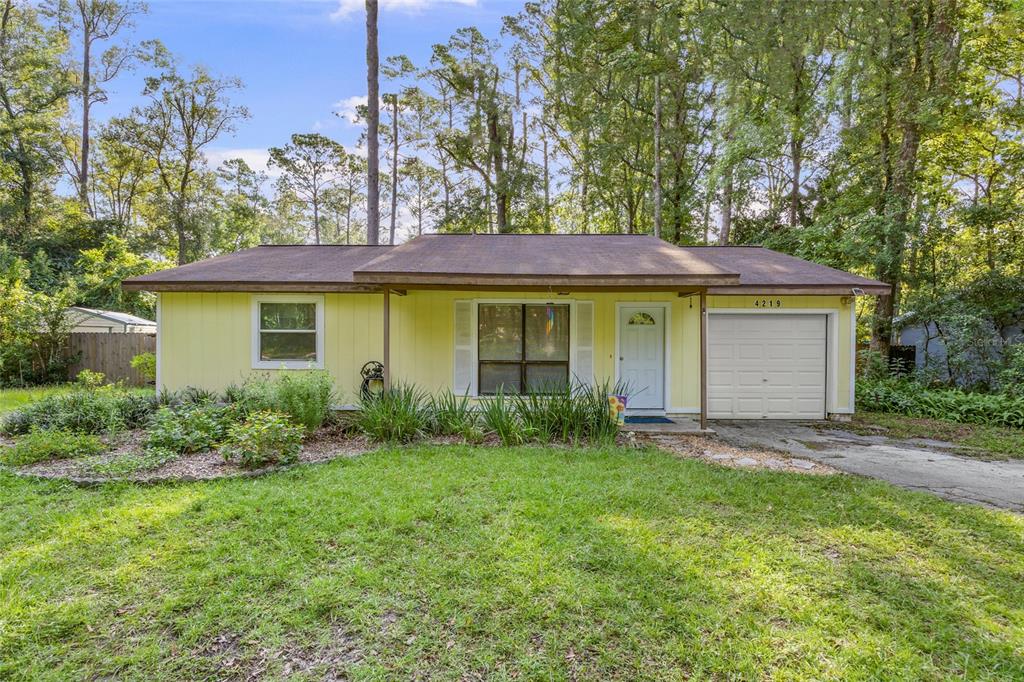 A single-story yellow house with a front-facing garage sits on a grassy lot with trees — 4219 NW 30TH TERRACE, GAINESVILLE, FL